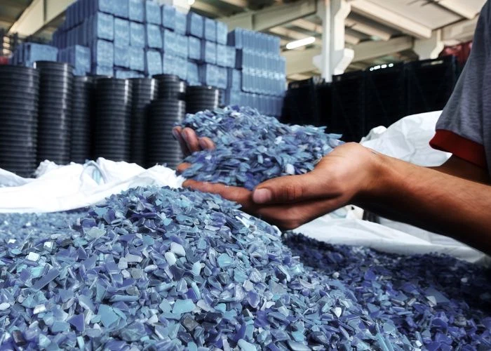 Worker holds newly produced blue-gray plastic material in hands to inspect and check the quality of plastic raw materials on production site