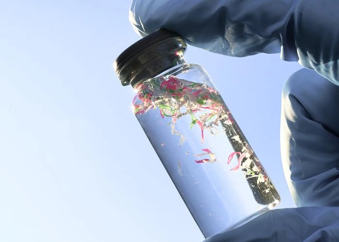 vibrant colorful microplastic particles stored inside a small transparent glass jar, sample of tiny plastic fragments from ocean pollution research