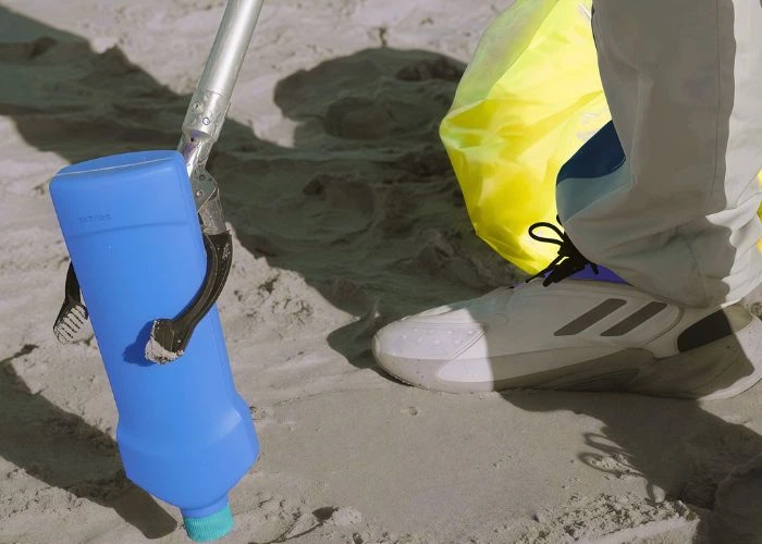 environmental protection worker picking up discarded blue plastic bottle litter on sandy beach shore, cleaning coastal plastic waste to protect marine environment
